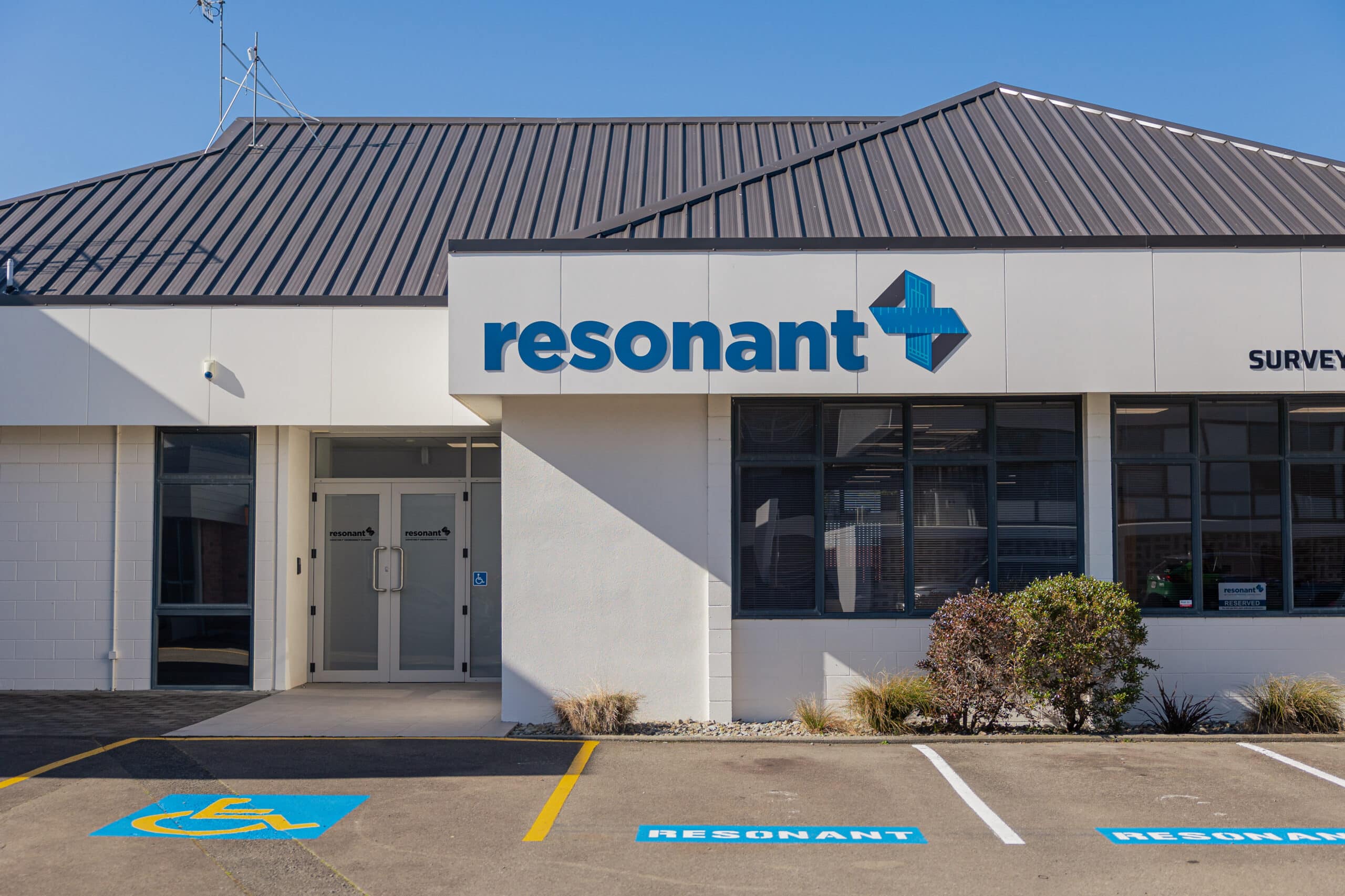 Front of a Resonant office building with a large blue logo and accessible parking spaces in the foreground.